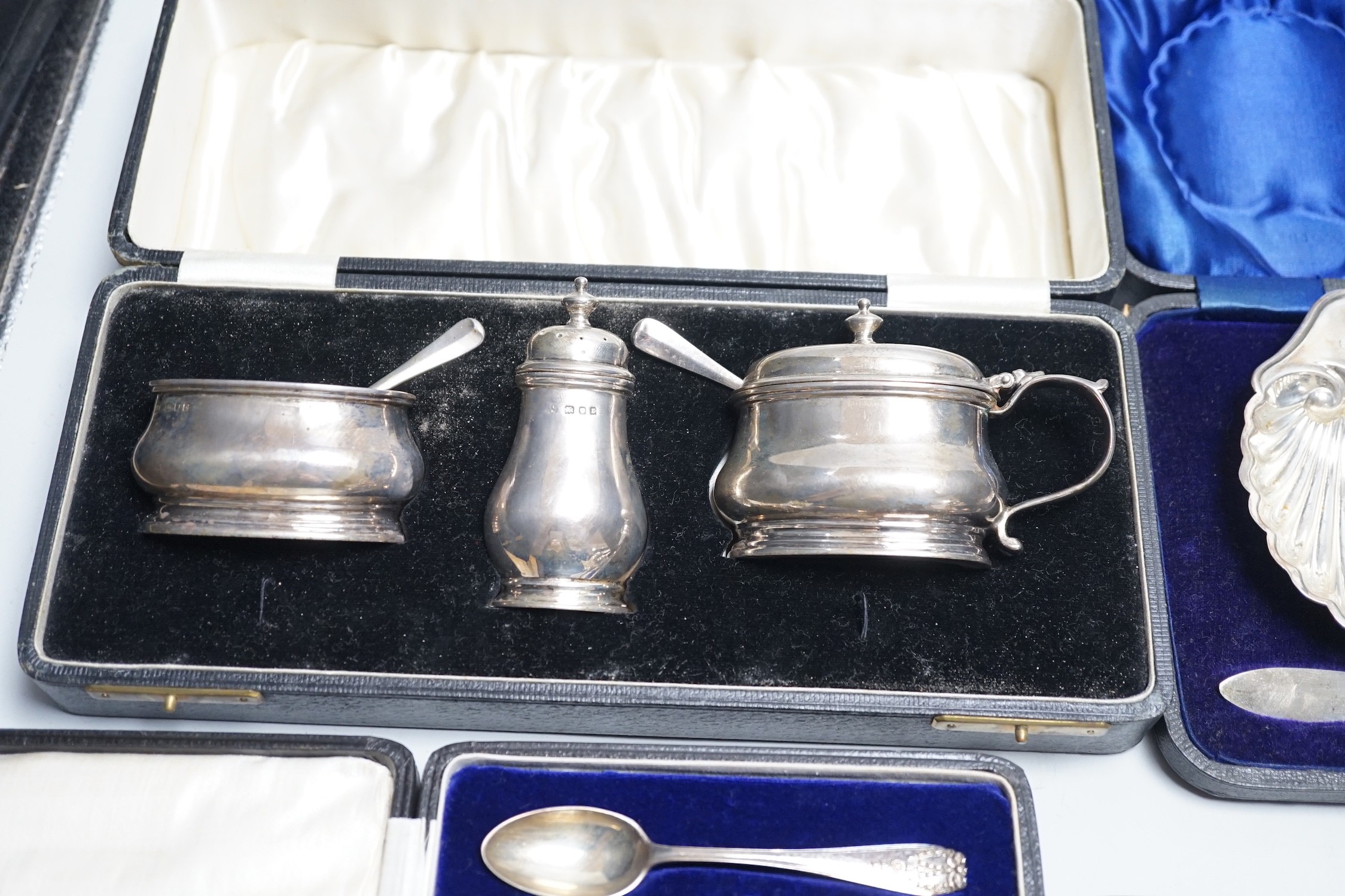 A quantity of mixed silver ware including a pair of modern candlesticks, 15cm, weighted, a cased George V three piece condiment set, cased butter shell and knife, two cased sets of teaspoons, a mounted photograph frame,